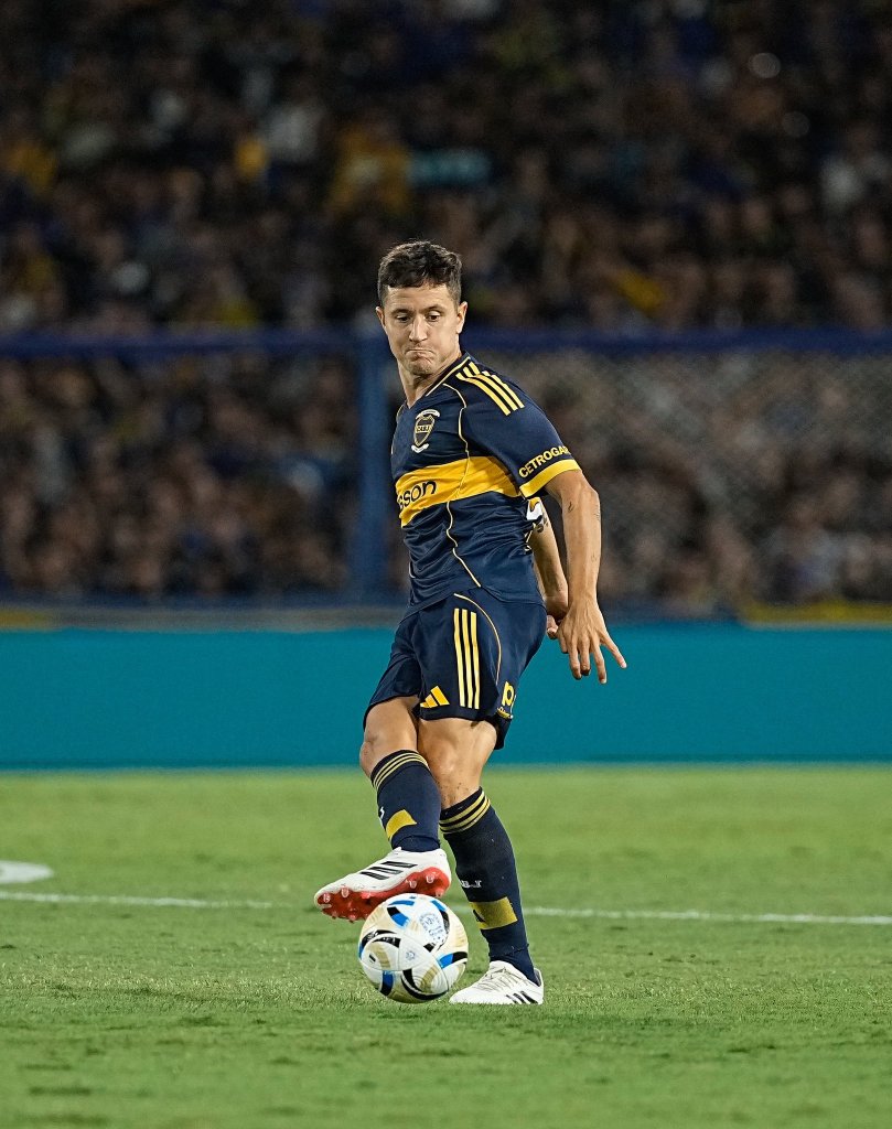 A soccer player is about to kick a ball on the field during a match, wearing a navy and yellow uniform.